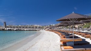 strand am meer mit sonnenliegen und kristallklaren azur blauen türkisen ozean wasser im hintergrund ein aussichtsturm aus stein alles gehört zum luxuriösen hochklassigen exklusiven designer hotel santa marina auf mykonos in griechenland europa